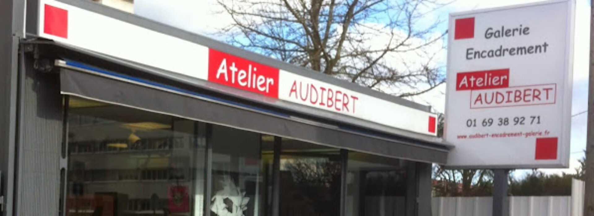 Façade d'une boutique d'encadrement et galerie nommée Atelier Audibert, avec son enseigne rouge et blanche et un panneau indiquant le numéro de téléphone.