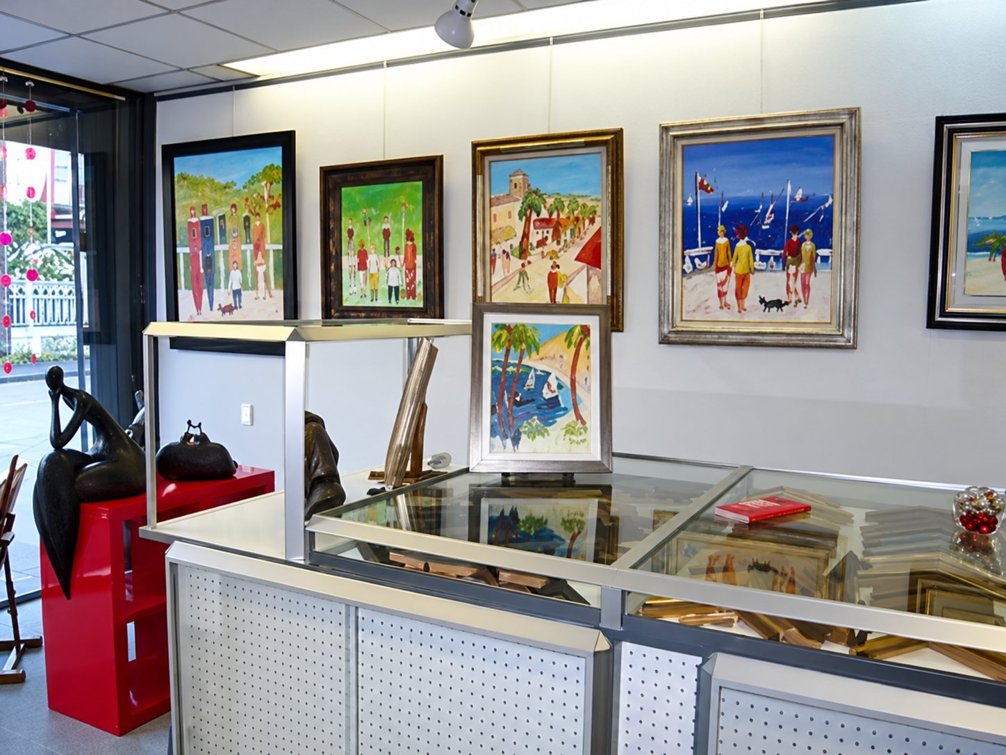 Intérieur d'une boutique avec plusieurs tableaux colorés accrochés au mur blanc et des vitrines en verre au premier plan.