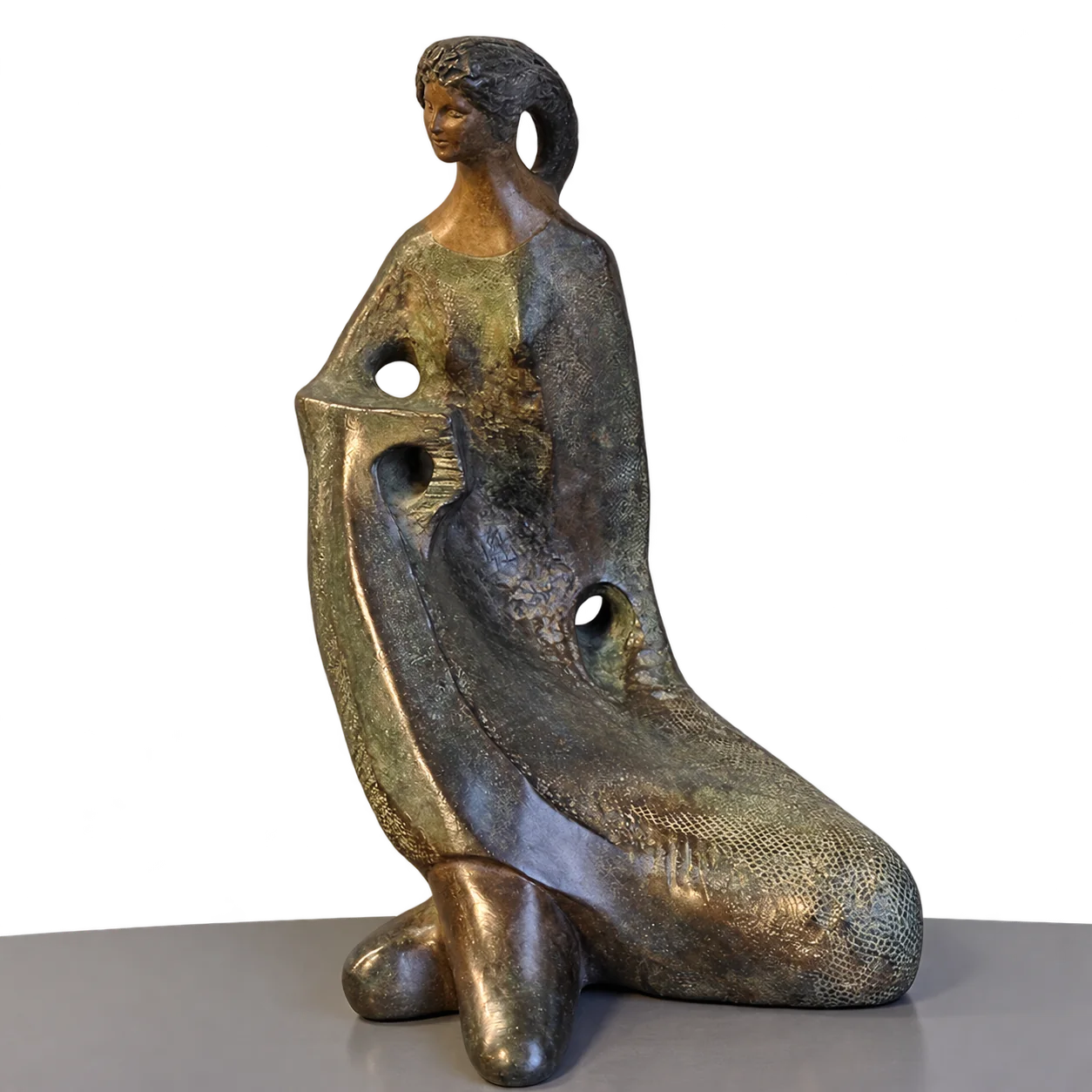 Sculpture en bronze à patine verte et brune représentant une femme assise, au drapé percé de trois ouvertures, posée sur une étagère grise devant un mur blanc crépi.