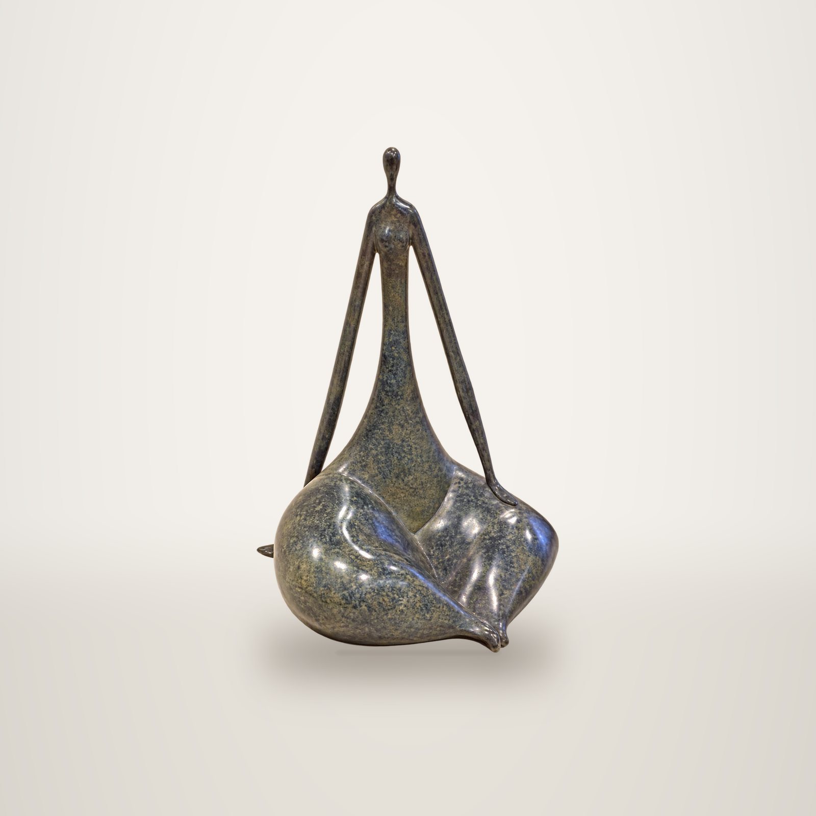 Sculpture en bronze à la patine gris-bleu représentant une figure féminine stylisée et assise, aux bras fins et au corps arrondi, posée devant un mur clair.