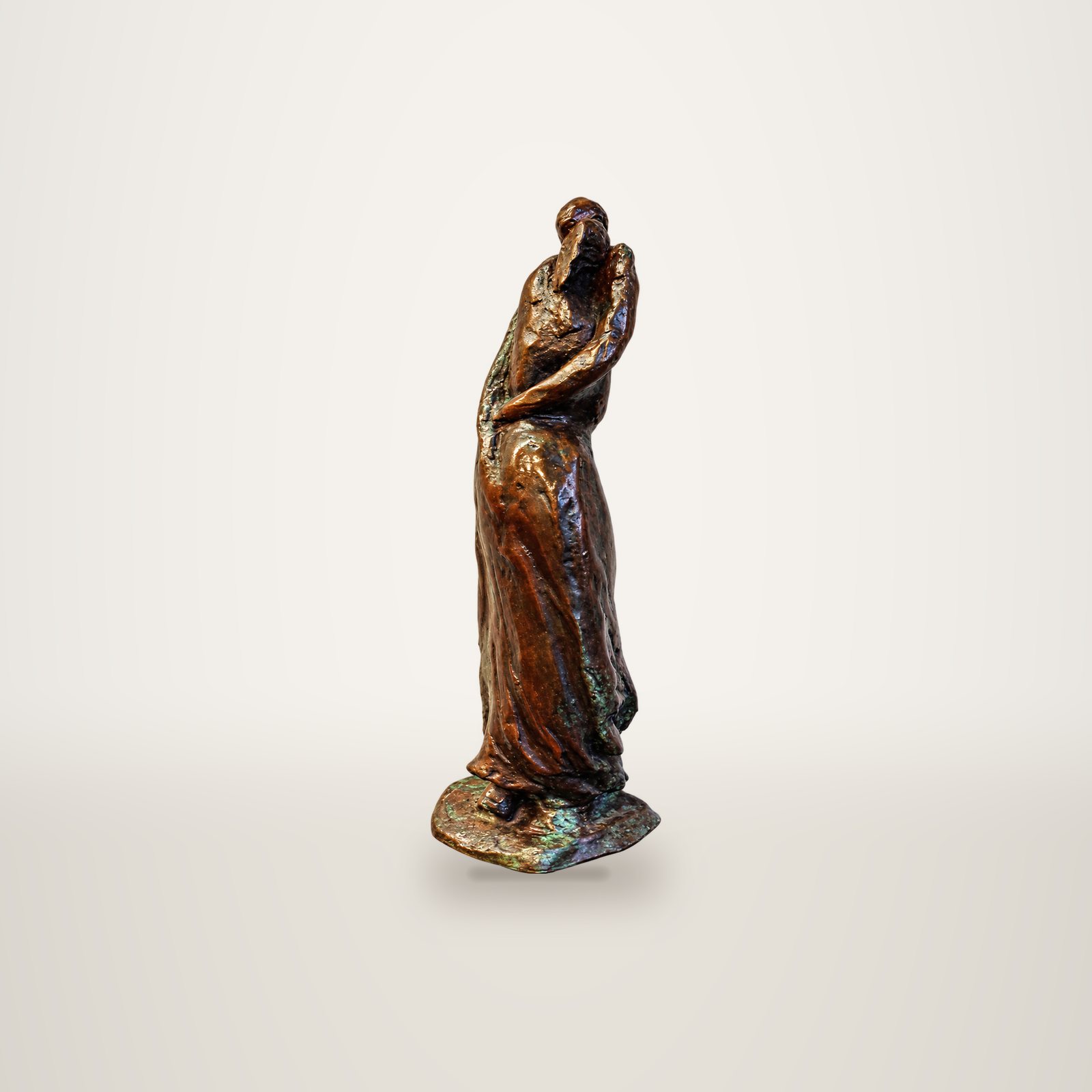 Une statuette en bronze à patine brune représentant une silhouette drapée, posée sur une surface grise devant un mur blanc crépi.